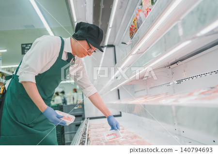 Upper body of a male employee sorting pork in the meat section of a supermarket. Upper body of a male employee sorting pork in the meat section of a supermarket. 140794693