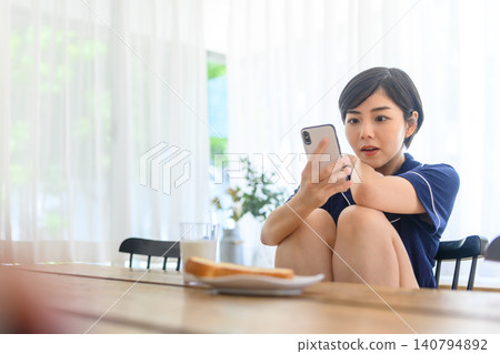 一個女人一邊吃早餐一邊看著她的智能手機 一個女人一邊吃早餐一邊看著她的智能手機 140794892