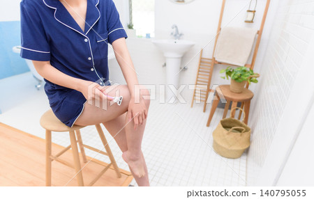 A woman sitting in a chair shaves the unwanted hair on her legs. A woman sitting in a chair shaves the unwanted hair on her legs. 140795055