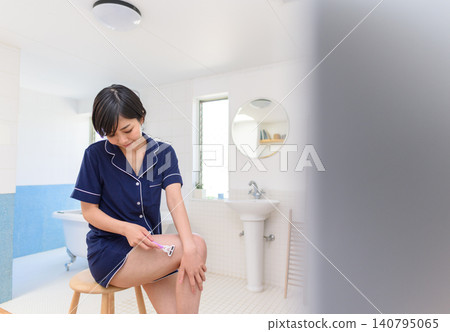 A woman removing unwanted leg hair in the bathroom. A woman removing unwanted leg hair in the bathroom. 140795065