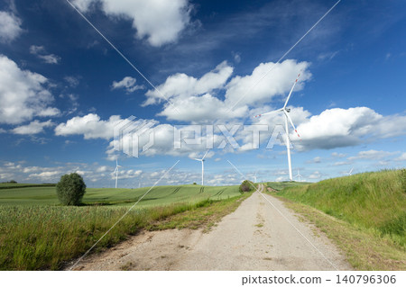 Wind turbines standing in a green field with a road and a clear sky Wind turbines standing in a green field with a road and a clear sky 140796306
