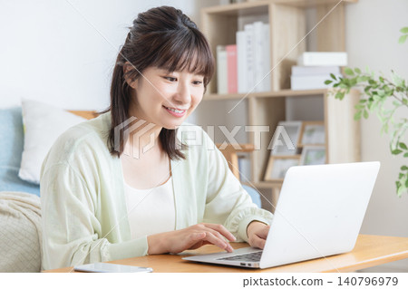 一位女士在家裡的客廳一邊使用電腦一邊微笑。 一位女士在家裡的客廳一邊使用電腦一邊微笑。 140796979