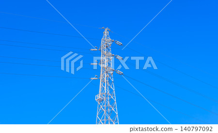A pure white power transmission tower and numerous power lines stand tall against a vibrant blue sky. A pure white power transmission tower and numerous power lines stand tall against a vibrant blue sky. 140797092