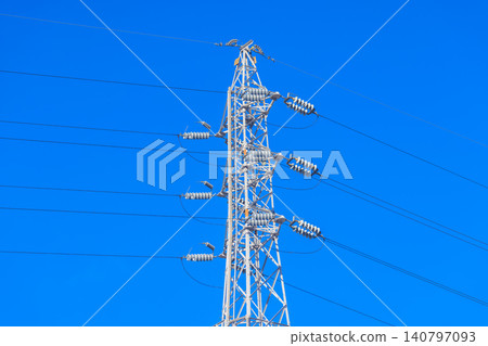 A pure white power transmission tower and numerous power lines stand tall against a vibrant blue sky. A pure white power transmission tower and numerous power lines stand tall against a vibrant blue sky. 140797093