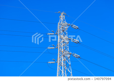 A pure white power transmission tower and numerous power lines stand tall against a vibrant blue sky. A pure white power transmission tower and numerous power lines stand tall against a vibrant blue sky. 140797094