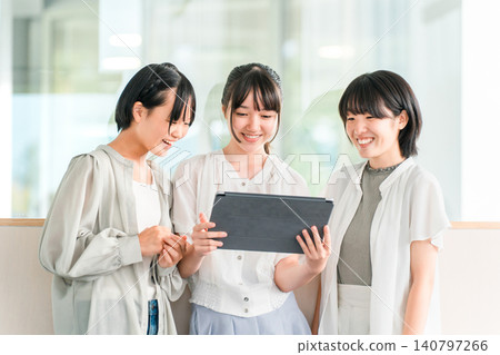 穿著休閒服的小學和國中女生和朋友們開心地看著平板電腦 穿著休閒服的小學和國中女生和朋友們開心地看著平板電腦 140797266