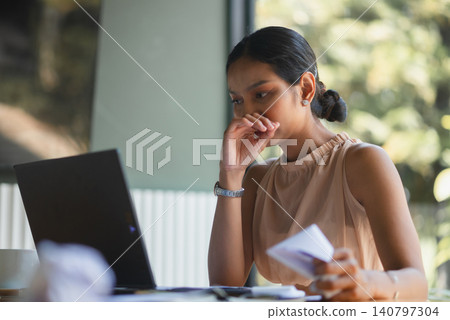 Worried businesswoman looking at laptop while holding paperwork in modern office, representing financial review, tax problem, budget planning, decision making, work stress, and business risk. Worried businesswoman looking at laptop while holding paperwork in modern office, representing financial review, tax problem, budget planning, decision making, work stress, and business risk. 140797304