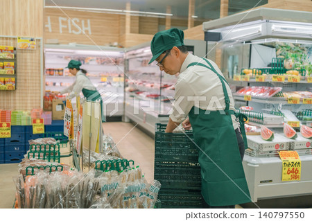 A male staff member in charge of produce at a supermarket is arranging the products on the shelves. 140797550
