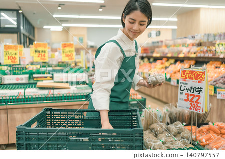 A female staff member in the produce section of a supermarket is working with products in her hands. A female staff member in the produce section of a supermarket is working with products in her hands. 140797557