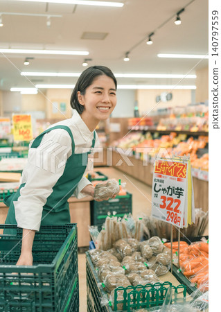 超市蔬果區的一名女店員面帶燦爛的笑容為顧客服務。 140797559