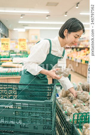 A female staff member in the produce section of a supermarket is picking up a potato. A female staff member in the produce section of a supermarket is picking up a potato. 140797562
