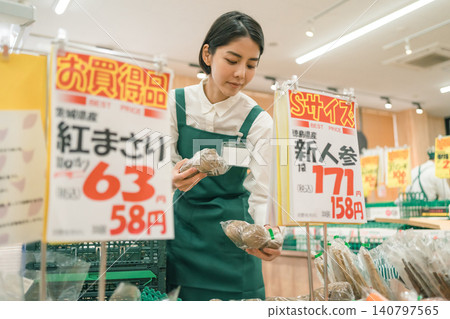 超市蔬果區的一名女員工正拿著一件商品,面前貼著價格標籤。 超市蔬果區的一名女員工正拿著一件商品,面前貼著價格標籤。 140797565