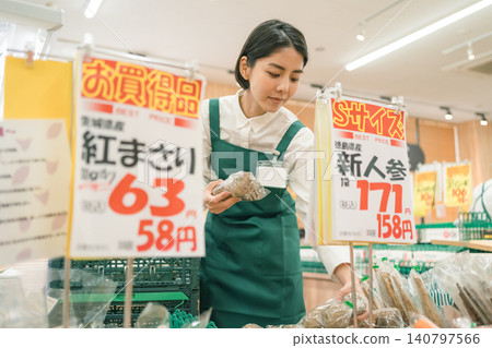 超市蔬果區的一名女員工正在檢查貼有價格標籤的商品。 140797566