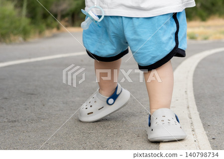 Close-up of a toddler taking first steps on an asphalt path outdoors Close-up of a toddler taking first steps on an asphalt path outdoors 140798734