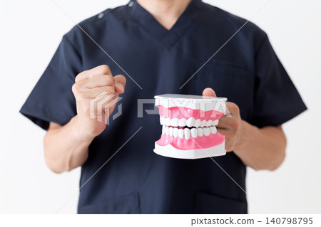 A middle-aged male dentist makes a triumphant gesture while holding a dental model. A middle-aged male dentist makes a triumphant gesture while holding a dental model. 140798795