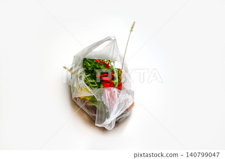 DEFOCUS. Plastic nature. Red and green plants flowers in a plastic bag on a white background. A dry blade of grass sticks out. Ecological problems. Out of focus DEFOCUS. Plastic nature. Red and green plants flowers in a plastic bag on a white background. A dry blade of grass sticks out. Ecological problems. Out of focus 140799047