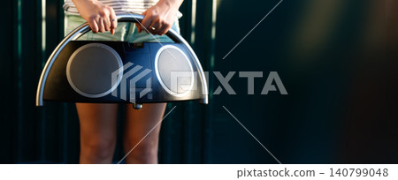 Young woman holding vintage boombox radio audio speaker system. Female in denim shorts carrying retro ghettoblaster tape recorder, outdoor studio banner with copy space Young woman holding vintage boombox radio audio speaker system. Female in denim shorts carrying retro ghettoblaster tape recorder, outdoor studio banner with copy space 140799048