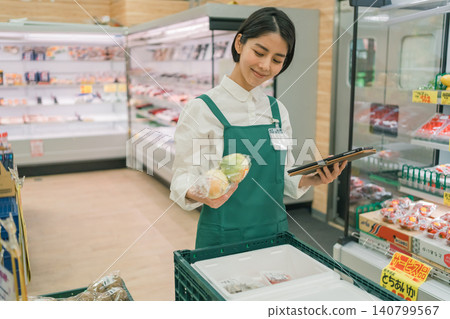 A female staff member at a supermarket uses a tablet to pick up orders for online grocery shopping. A female staff member at a supermarket uses a tablet to pick up orders for online grocery shopping. 140799567