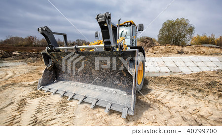 Universal excavator loader is seen on a construction site moving dirt and preparing the ground for future building work under a cloudy sky Universal excavator loader is seen on a construction site moving dirt and preparing the ground for future building work under a cloudy sky 140799700