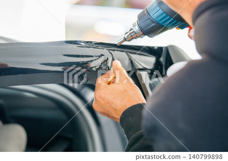A car wrapping specialist applies a polyurethane film to the car. Detailer PPF A car wrapping specialist applies a polyurethane film to the car. Detailer PPF 140799898