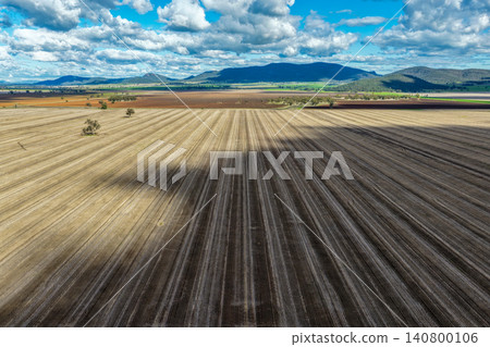 Aerial view of a cultivated field in the Namoi Valley with a mountain range beneath a dramatic cloudy sky, showcasing the expansive rural landscape of NSW, Australia. 140800106