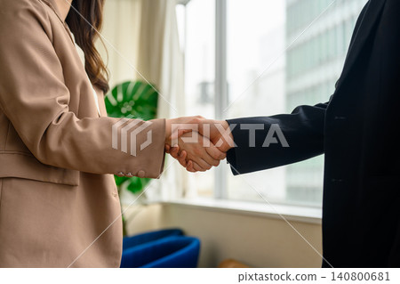 辦公室裡,一男一女兩位商務人士握手。 辦公室裡,一男一女兩位商務人士握手。 140800681