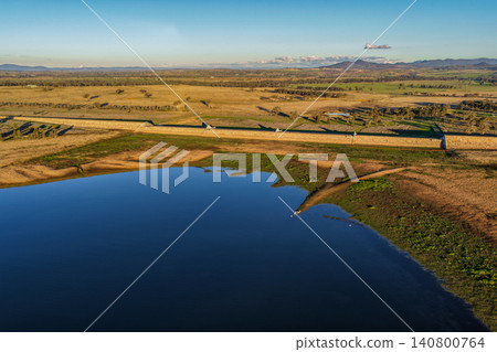 Aerial view showcasing the Lake Keepit earth embankment and surrounding rural landscape, highlighting the scale of the reservoir and the engineering features of the dam in NSW, Australia. Aerial view showcasing the Lake Keepit earth embankment and surrounding rural landscape, highlighting the scale of the reservoir and the engineering features of the dam in NSW, Australia. 140800764