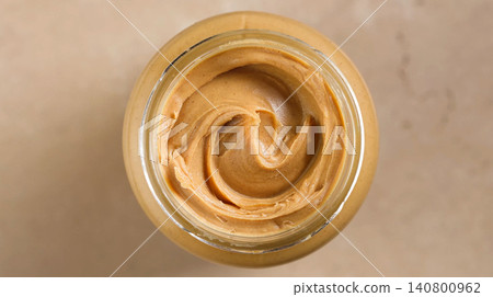Open Jar of Peanut Butter on Warm Beige Background, Top View 140800962