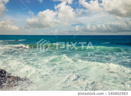 Sea wave foam on the rocky beach. Ocean wave on the beach. Coast on a sunny day. Windy weather Sea wave foam on the rocky beach. Ocean wave on the beach. Coast on a sunny day. Windy weather 140802983