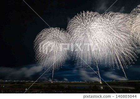 兩枚巨大的白色煙火並排在夜空中綻放,形成了一場奇幻而動感的煙火表演。 兩枚巨大的白色煙火並排在夜空中綻放,形成了一場奇幻而動感的煙火表演。 140803044