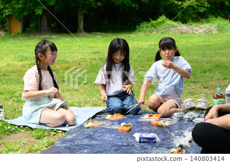 一群小學生在綠樹環繞的公園廣場上鋪上野餐毯,互相問候後開始用餐。 一群小學生在綠樹環繞的公園廣場上鋪上野餐毯,互相問候後開始用餐。 140803414