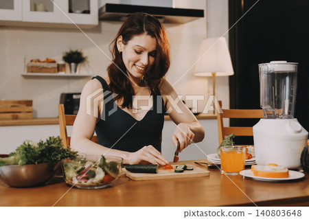 Woman preparing green smoothie in bright kitchen with fresh fruits and vegetables, healthy eating lifestyle moment in natural daylight 140803648