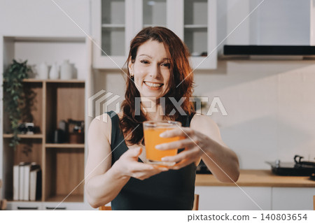 Woman preparing green smoothie in bright kitchen with fresh fruits and vegetables, healthy eating lifestyle moment in natural daylight 140803654