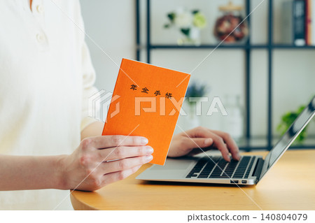 A young woman using a computer while holding her pension book. A young woman using a computer while holding her pension book. 140804079