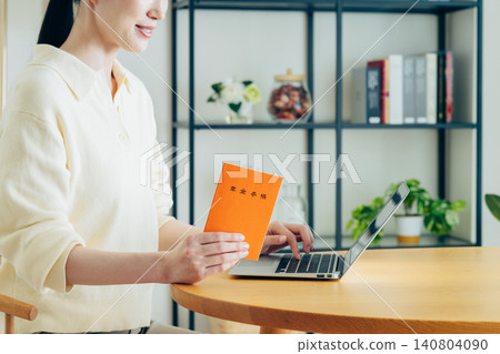 A young woman using a computer while holding her pension book. A young woman using a computer while holding her pension book. 140804090