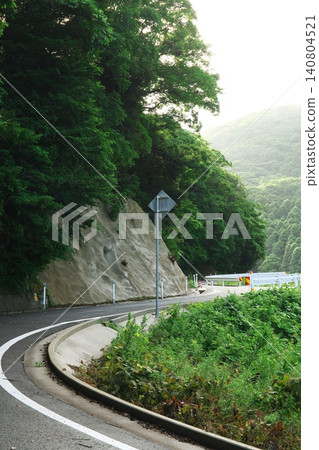 A winding road through the mountains during the rainy season, surrounded by beautiful greenery. A winding road through the mountains during the rainy season, surrounded by beautiful greenery. 140804521