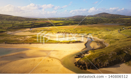 A vast green landscape of fields and hills meets the sea, with a small village nestled on the coastline. A vast green landscape of fields and hills meets the sea, with a small village nestled on the coastline. 140806512