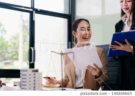 Two Asian female lawyers assist a client with a property dispute, reviewing legal documents and providing professional legal consultation. 140806663