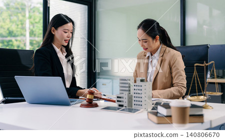Two Asian women lawyers review real estate contracts with a model house, property law, investment, legal advice, and consultation concepts. Two Asian women lawyers review real estate contracts with a model house, property law, investment, legal advice, and consultation concepts. 140806670