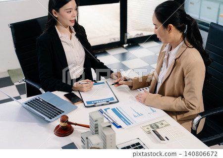 Two Asian women lawyers review real estate contracts with a model house, property law, investment, legal advice, and consultation concepts. Two Asian women lawyers review real estate contracts with a model house, property law, investment, legal advice, and consultation concepts. 140806672