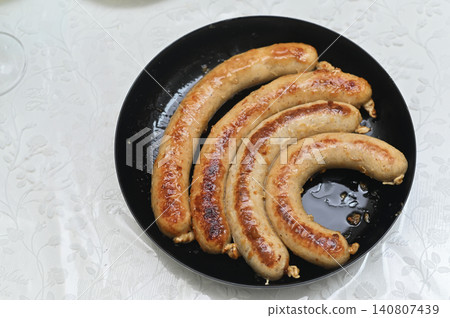 Roasted meat sausages lie inside black frying pan on table. 140807439