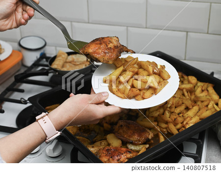 Woman holds dish with golden potatoes over oven baking sheet. Woman holds dish with golden potatoes over oven baking sheet. 140807518