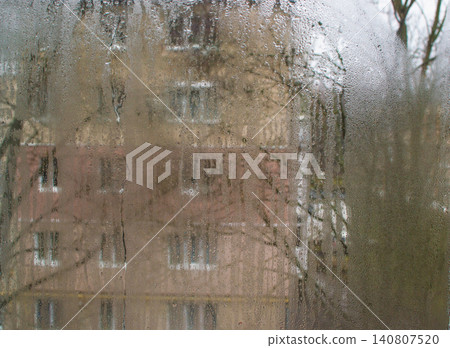 Wet glass covered by droplets and flowing drops of water lines. glass showing blurred house facade beyond. Wet window forms soft abstract backdrop, overcast atmosphere, weather concept, texture detail Wet glass covered by droplets and flowing drops of water lines. glass showing blurred house facade beyond. Wet window forms soft abstract backdrop, overcast atmosphere, weather concept, texture detail 140807520
