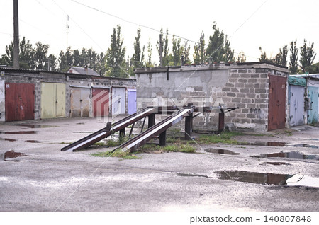 Grungy garage row looks desolated in Eastern Europe city. Metal car ramp structure serves for DIY auto service. Dilapidated property, block storage units and vintage architecture. Grungy garage row looks desolated in Eastern Europe city. Metal car ramp structure serves for DIY auto service. Dilapidated property, block storage units and vintage architecture. 140807848