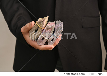 Businessman in black suit holds three rolls of money in one hand. Businessman in black suit holds three rolls of money in one hand. 140807850