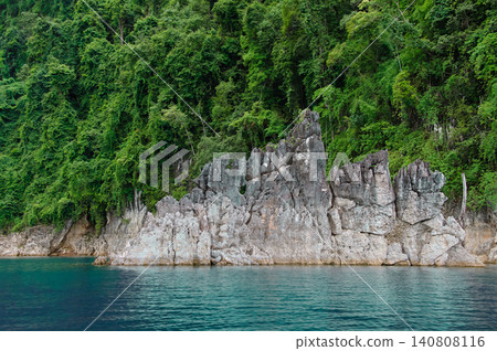 Rocky mountains, lush with trees, rise from the azure water, their cliffs catching the afternoon sun, set against a sky filled with clouds. Rocky mountains, lush with trees, rise from the azure water, their cliffs catching the afternoon sun, set against a sky filled with clouds. 140808116