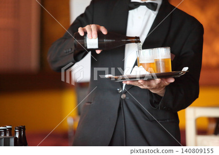 標題:派對場所中,一名男服務生將啤酒倒入托盤上的玻璃杯中。 標題:派對場所中,一名男服務生將啤酒倒入托盤上的玻璃杯中。 140809155