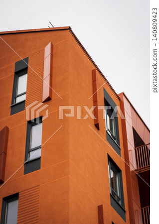 Abstract close-up view of a modern bright orange apartment building corner with geometric window frames and minimalist architectural details. 140809423