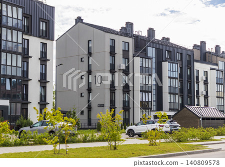 Modern scandinavian-style residential block with contemporary low-rise cityhouses, street parking lot, and landscaped courtyard under a cloudy summer sky. Modern scandinavian-style residential block with contemporary low-rise cityhouses, street parking lot, and landscaped courtyard under a cloudy summer sky. 140809578