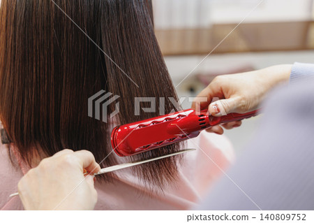 Using a red curling iron and comb to straighten a woman's hair. Using a red curling iron and comb to straighten a woman's hair. 140809752